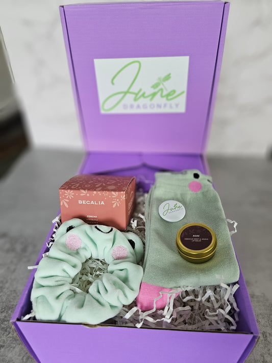 Purple June Dragonfly gift box that features Becalia Botanicals Hibiscus Nourishing Clay Mask, Mint and Apple Froggy Socks, Mint and Apple Froggy Scrunchie, Becalia Botanicals Rebe Hibiscus Mint + Agave Lip Balm and June Dragonfly pin