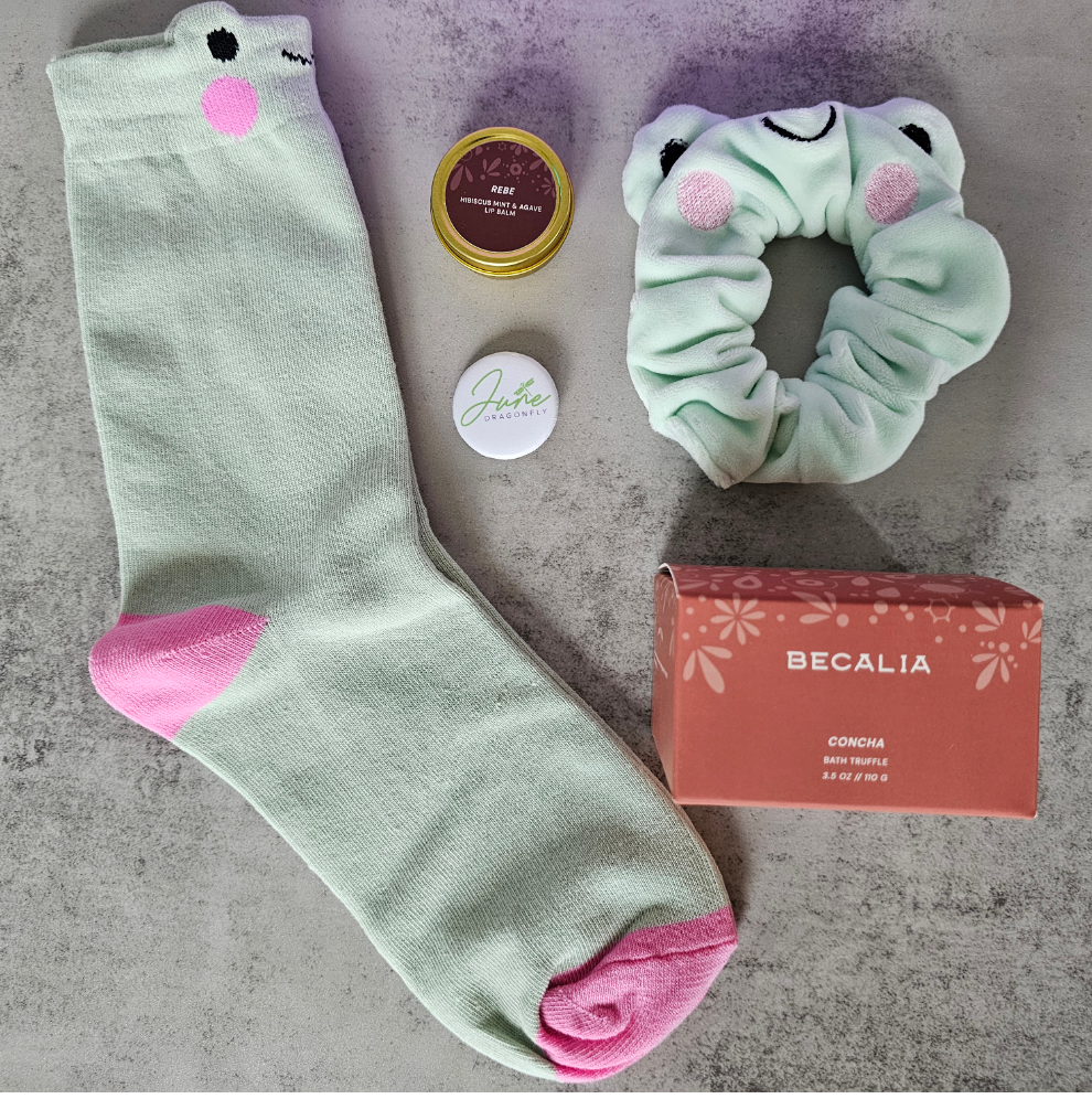 Purple June Dragonfly gift box contents: Becalia Botanicals Hibiscus Nourishing Clay Mask, Mint and Apple Froggy Socks, Mint and Apple Froggy Scrunchie, Becalia Botanicals Rebe Hibiscus Mint + Agave Lip Balm and June Dragonfly pin